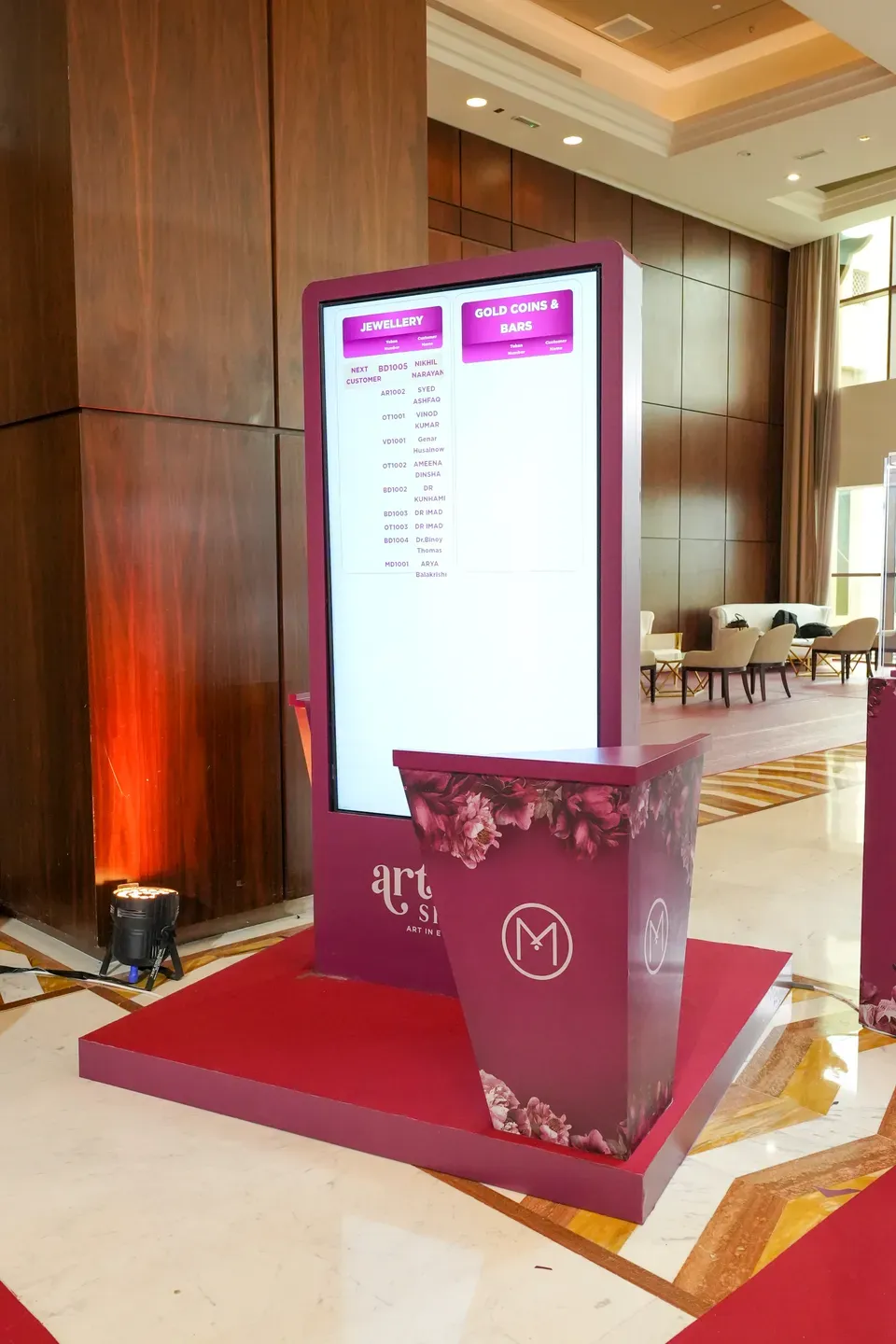 Burgundy digital totem showing a programme schedule on a red carpet plinth