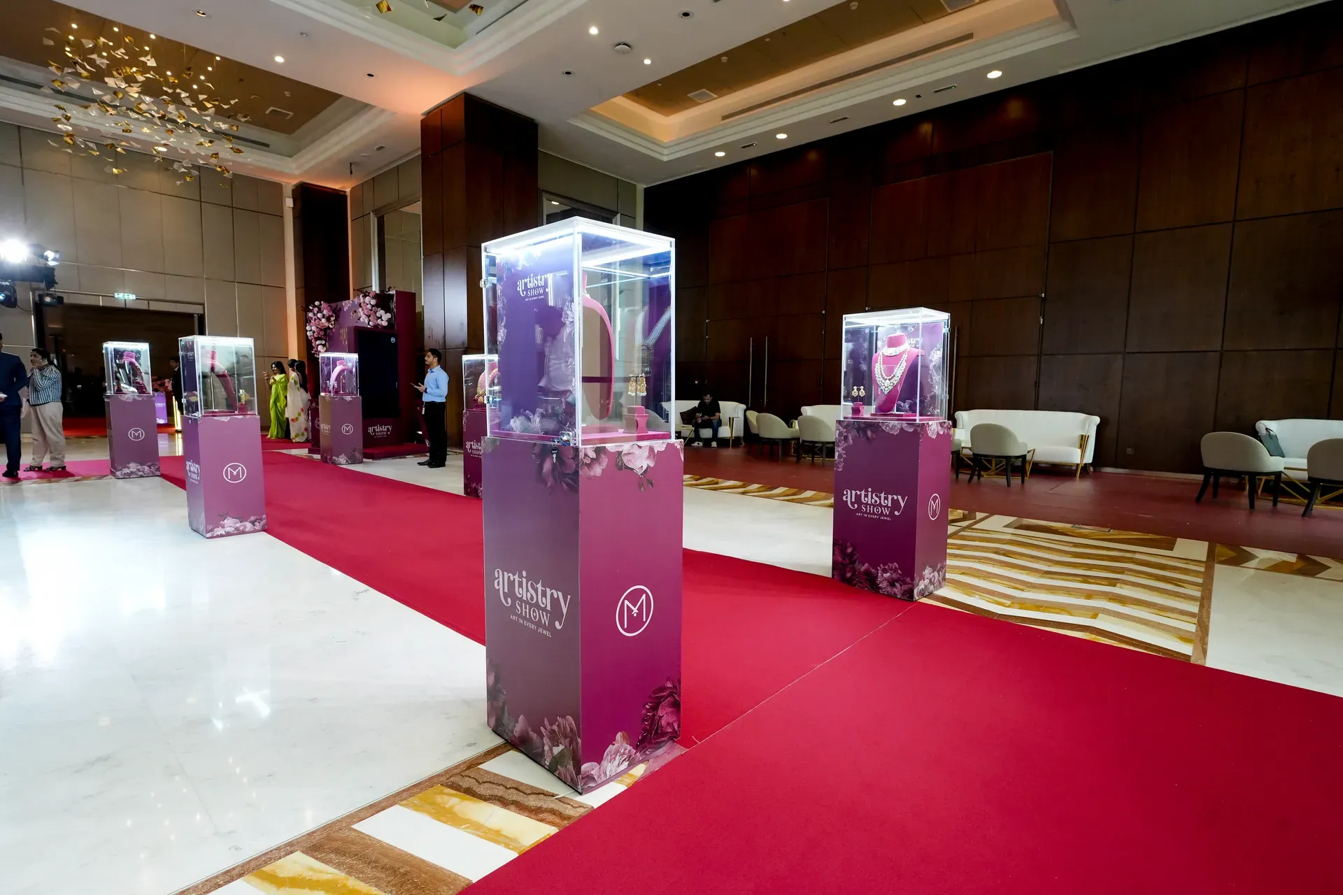 Row of lit glass display cases on branded plinths down a red carpet runner