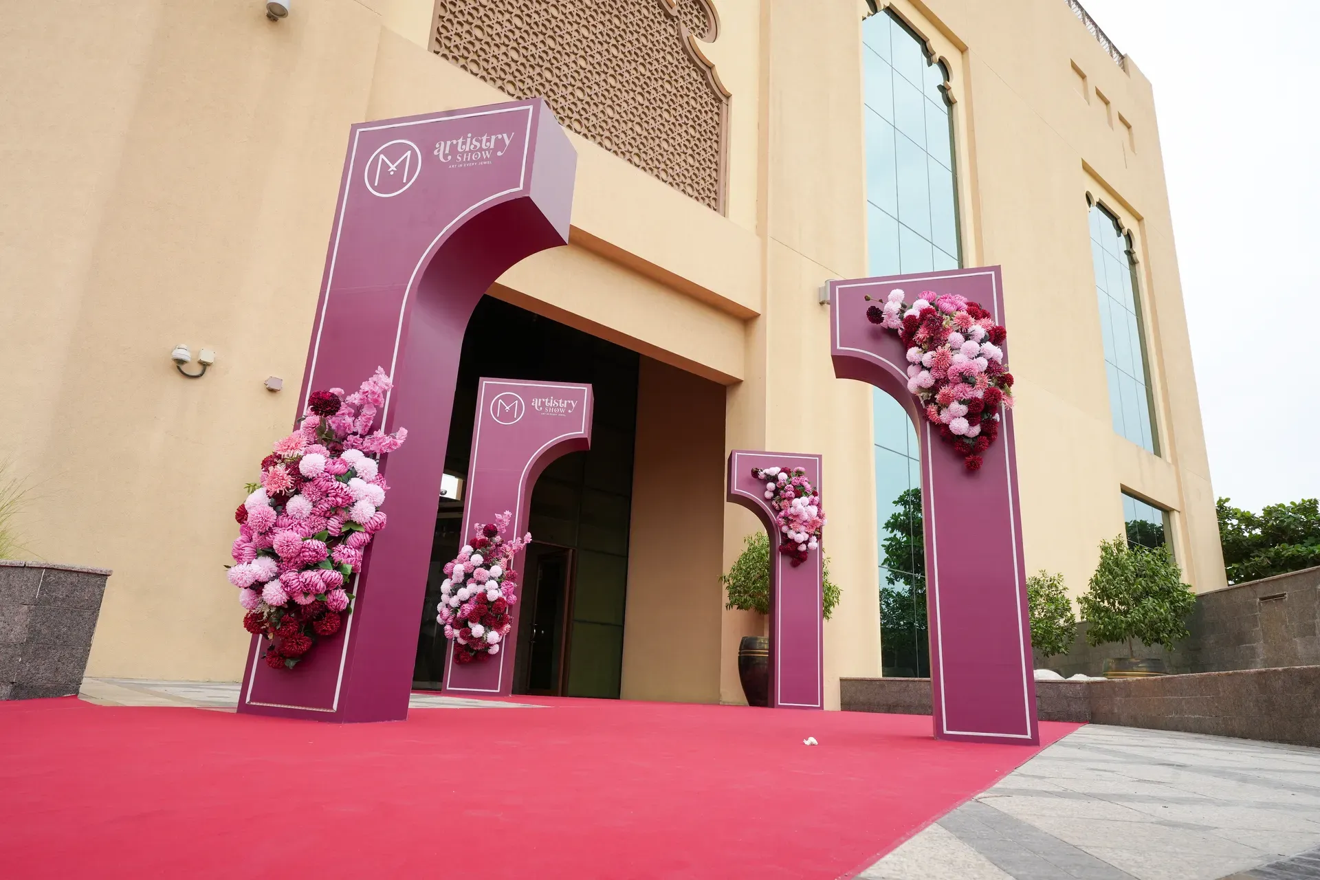Curved burgundy arches dressed with pink florals framing a glass hotel doorway