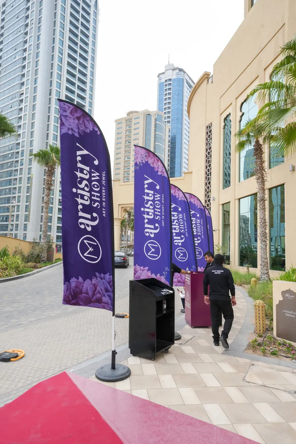 Purple feather flags lining a pavement outside a hotel beside a pink carpet