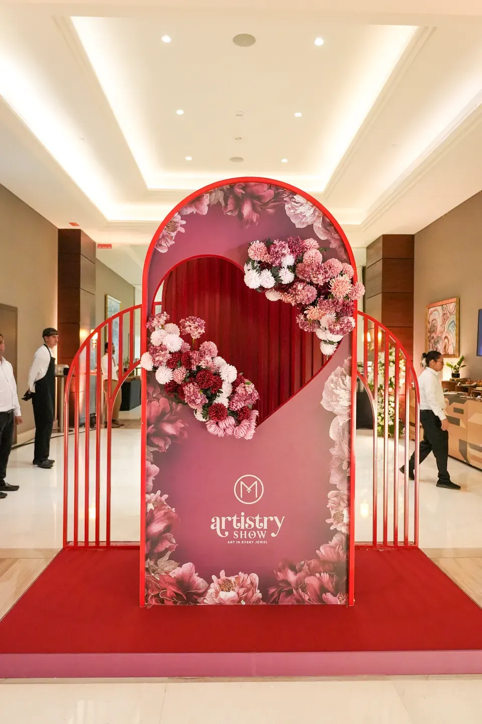 Red arch with a floral heart opening standing on a red carpet in a hotel lobby