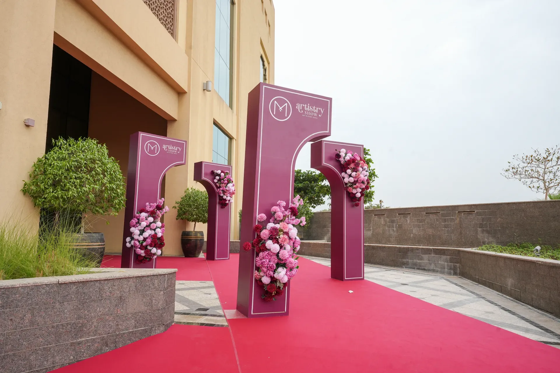 Row of burgundy branded totems with floral clusters seen low along a red carpet