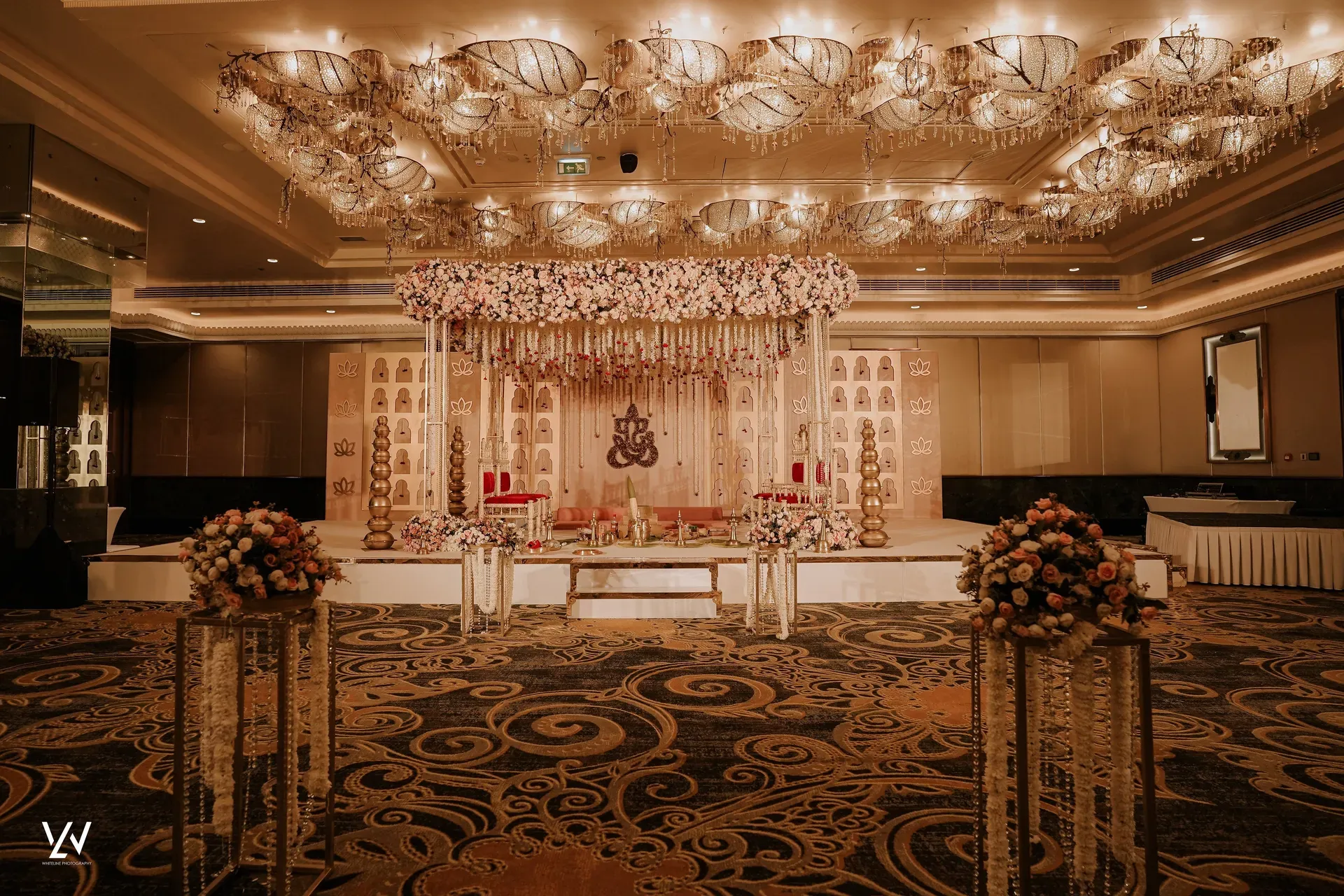 Ballroom stage framed by a canopy of suspended pink and white florals above a mandap