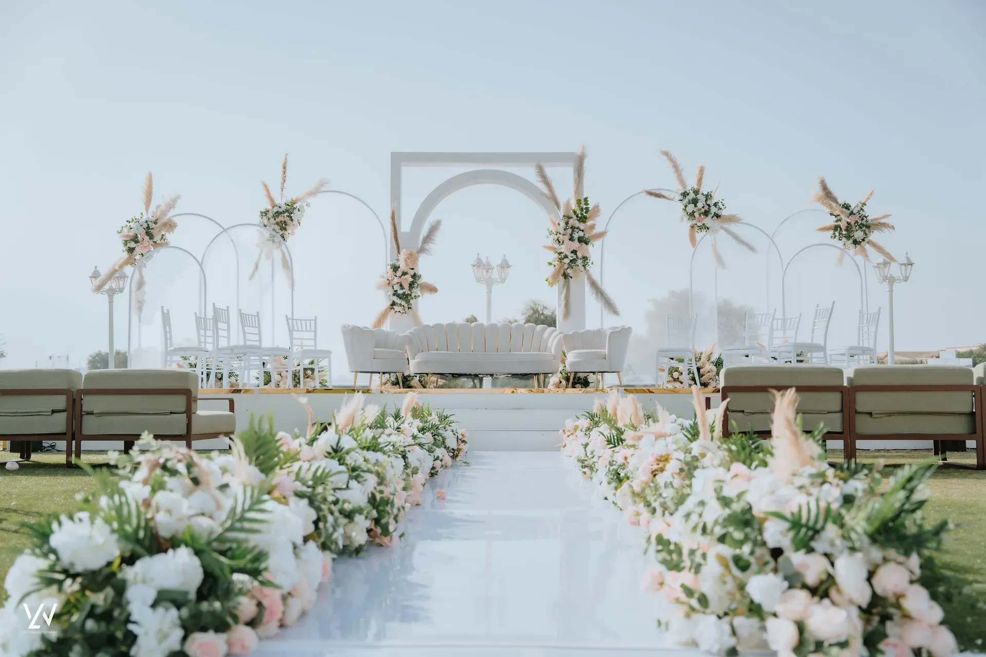 White ceremony aisle to a square arch flanked by pampas grass and blush floral beds