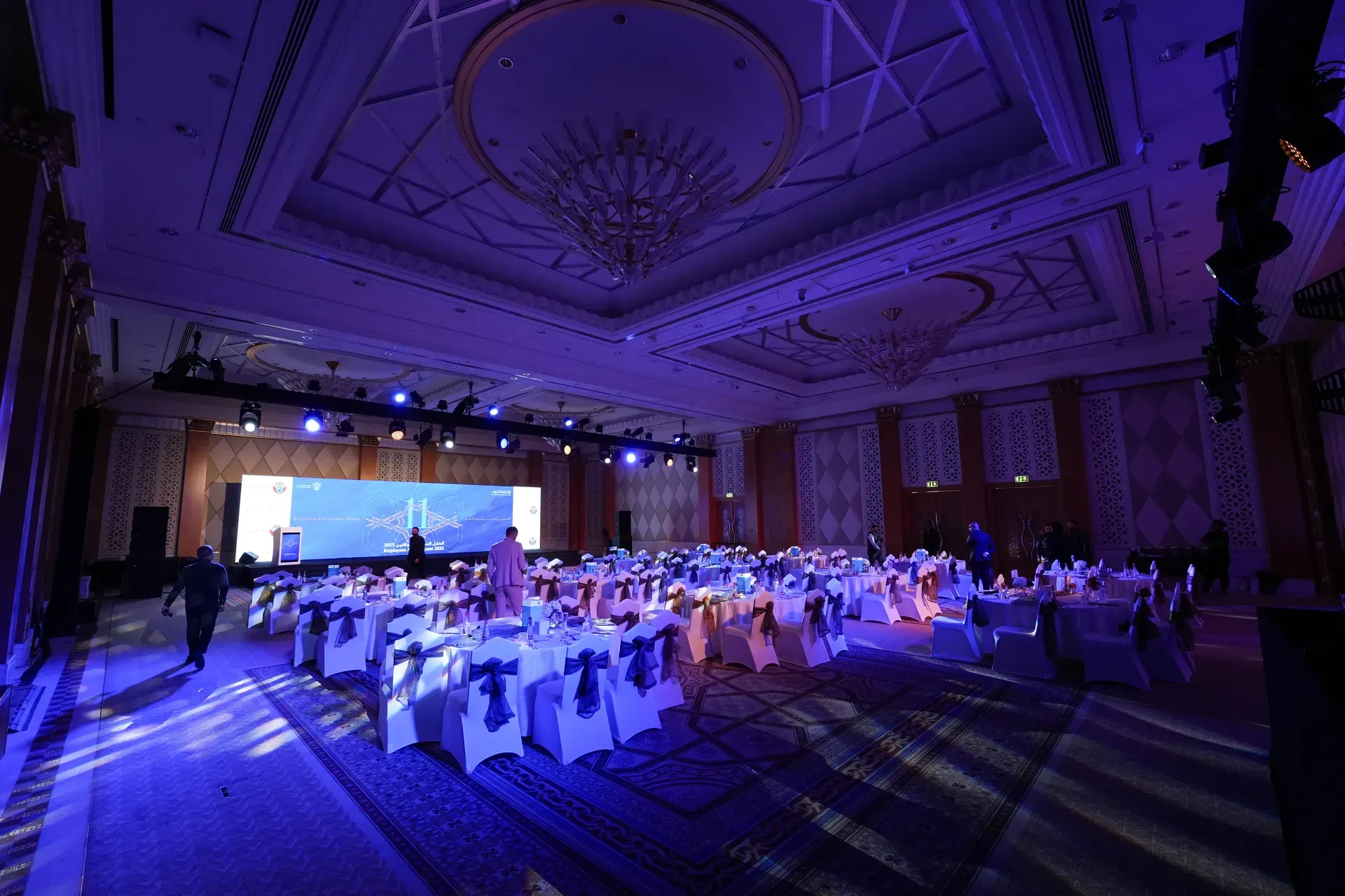 Blue-lit banquet hall seen along its side aisle beneath a domed chandelier