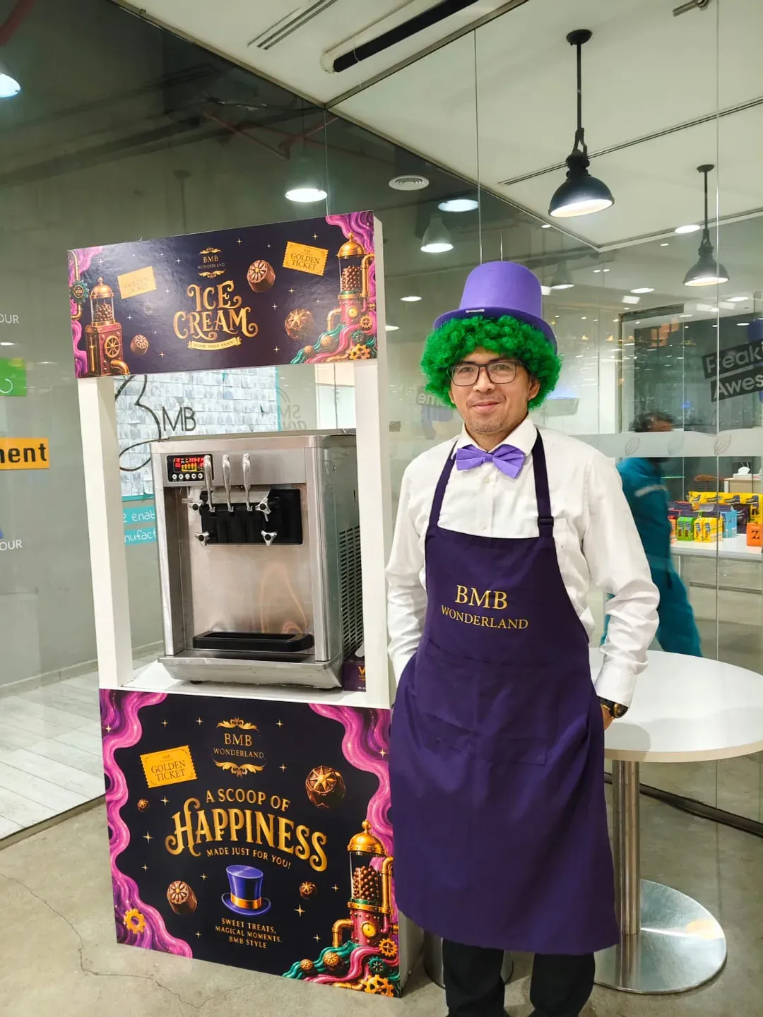 Host in a purple apron and top hat standing beside a branded ice cream cart