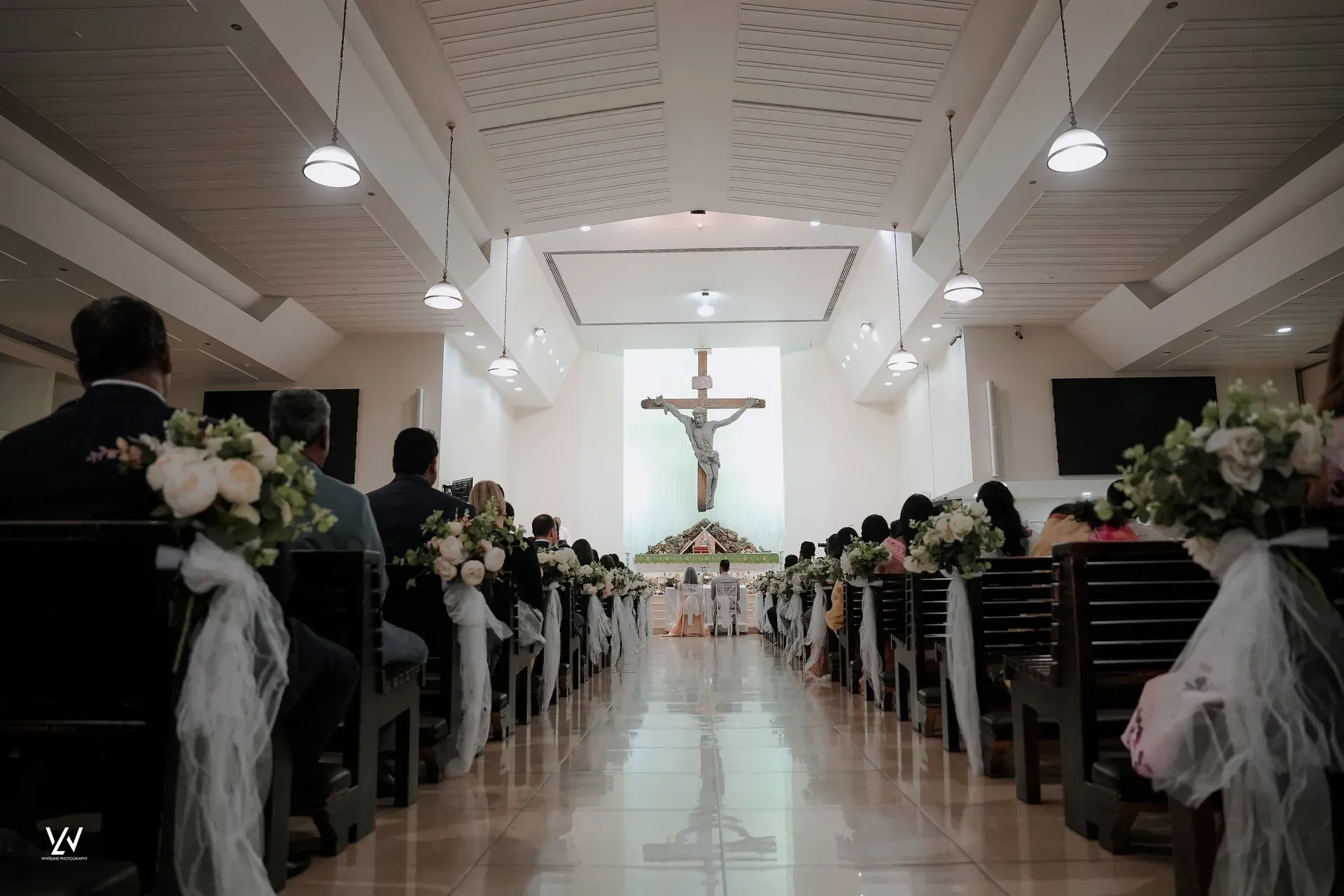 Church aisle lined with white rose and eucalyptus pew arrangements tied in tulle