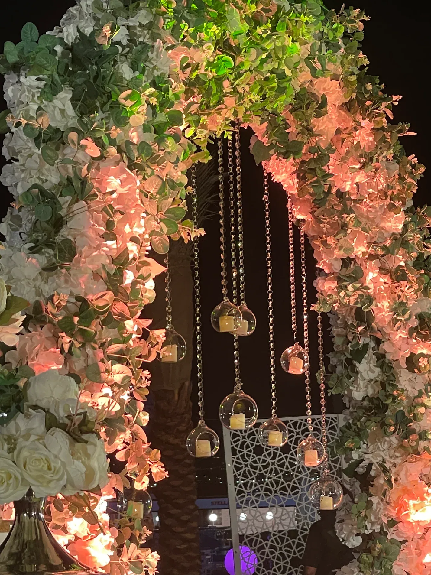Close view of the floral arch, with glass globes holding lit candles hanging on beaded strands