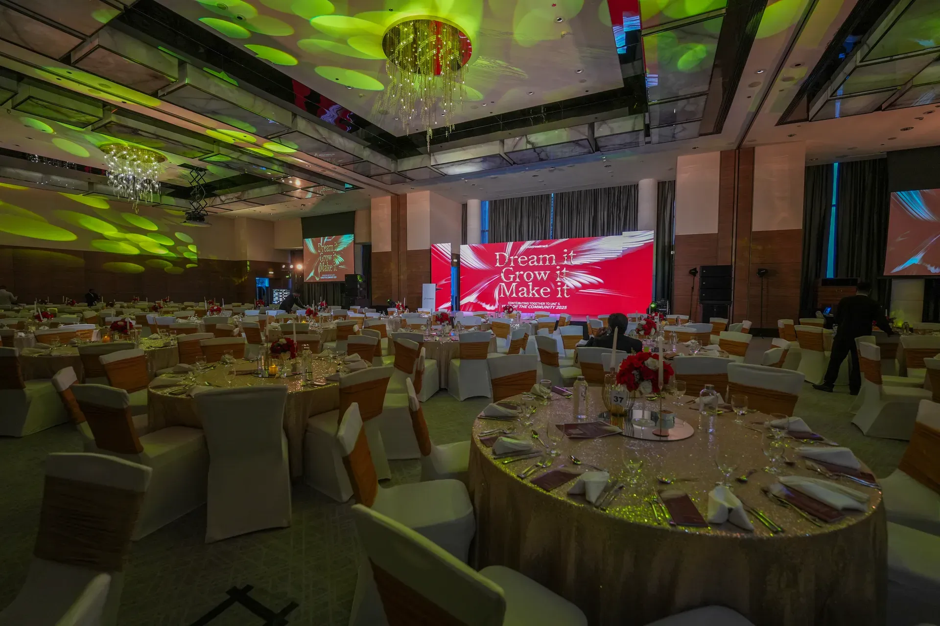 Banquet tables in gold linen with low floral centrepieces under patterned lighting