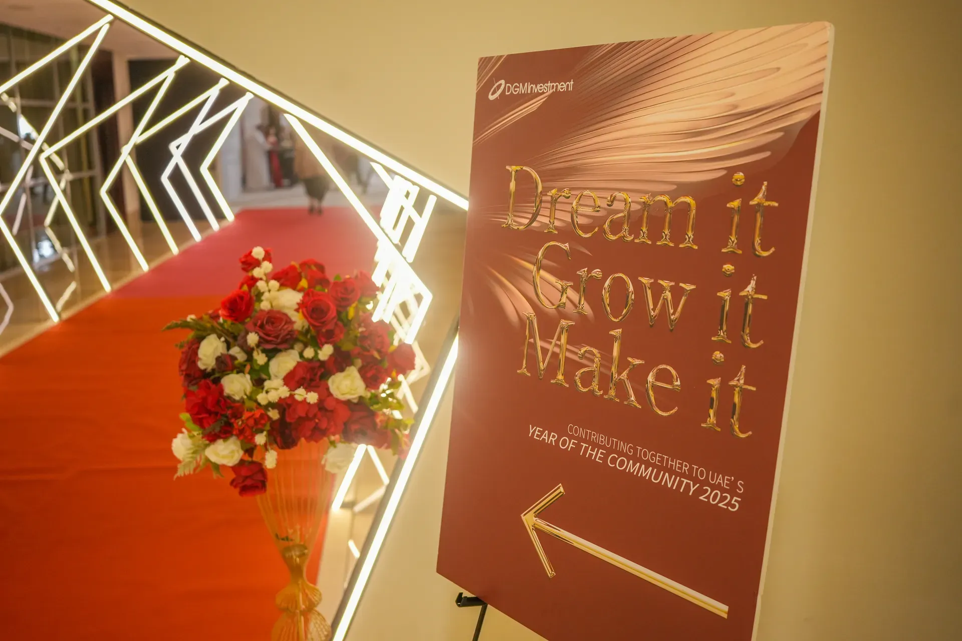 Burgundy welcome sign in gold lettering beside a red and white floral arrangement