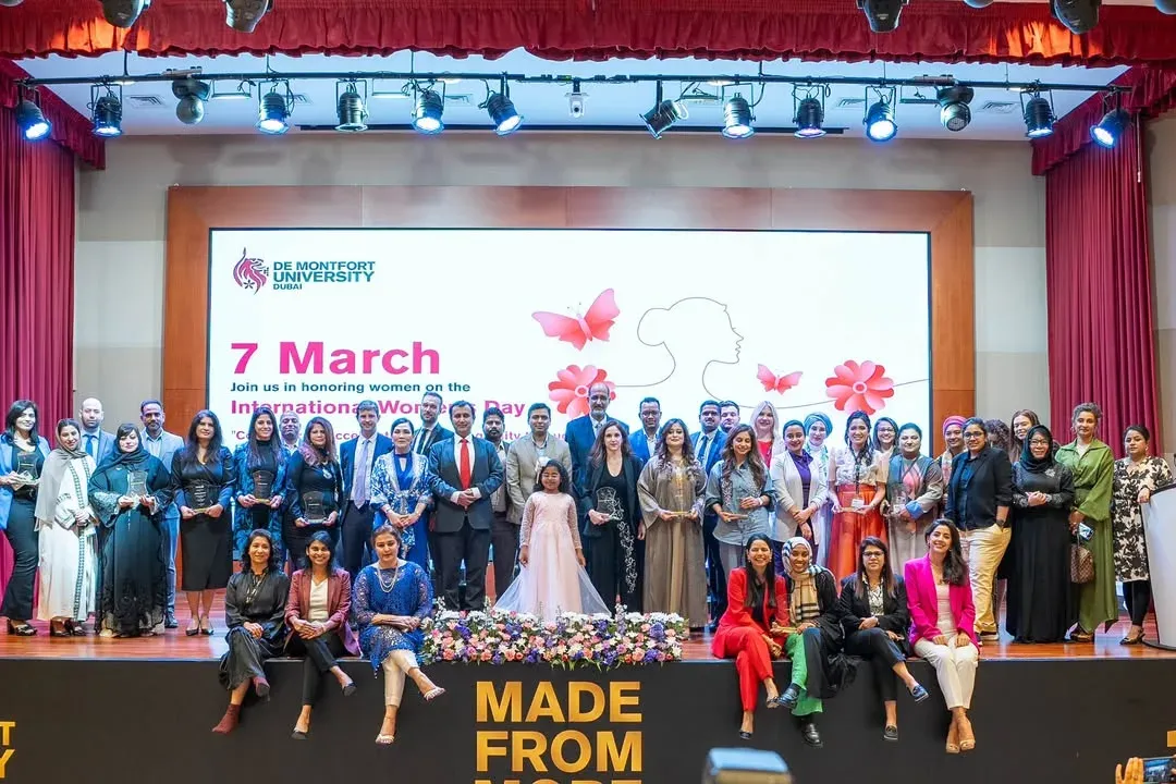 Large group photographed on an auditorium stage in front of an International Women's Day screen