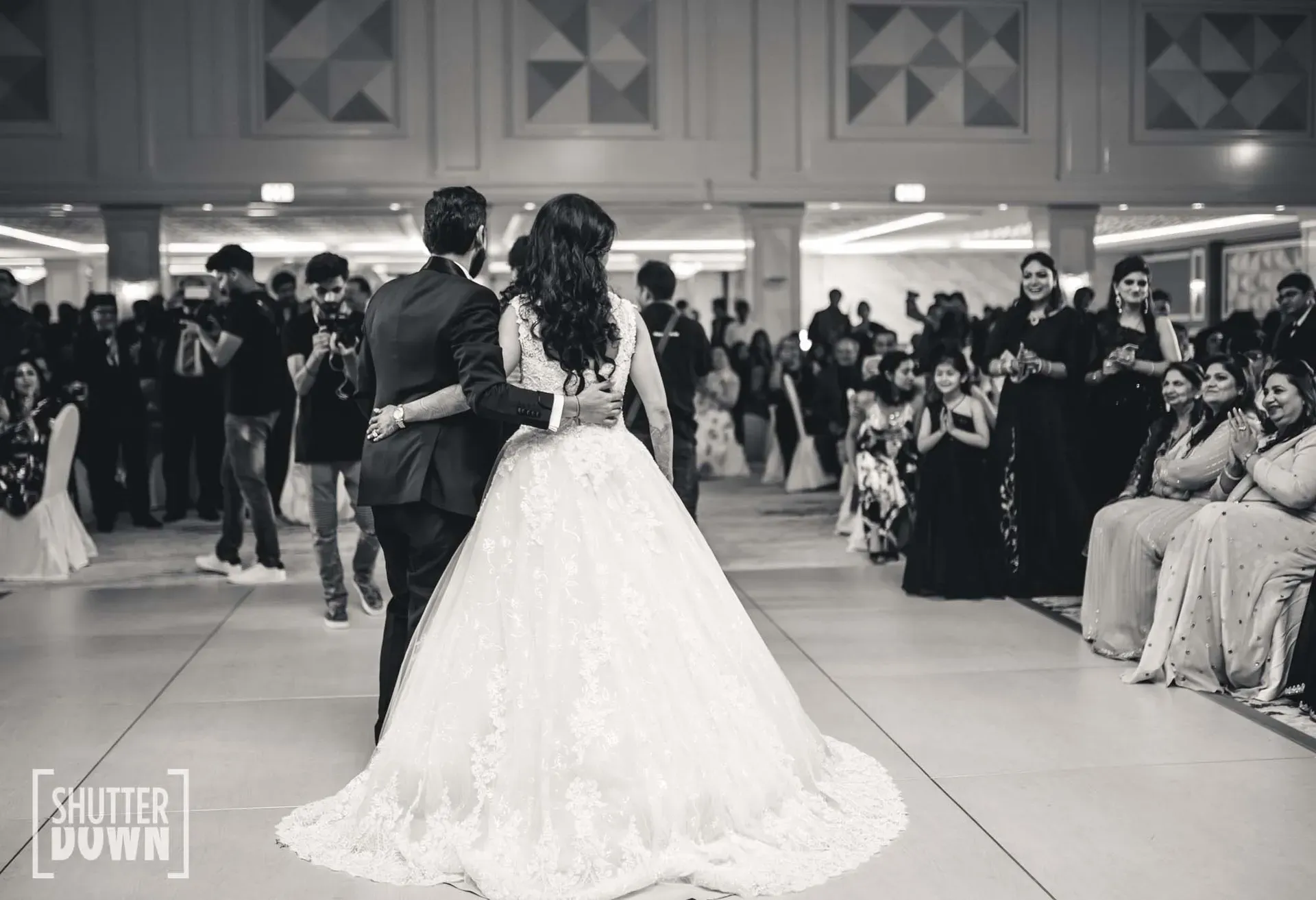 Black and white frame of a couple dancing as guests watch from the edge of the floor