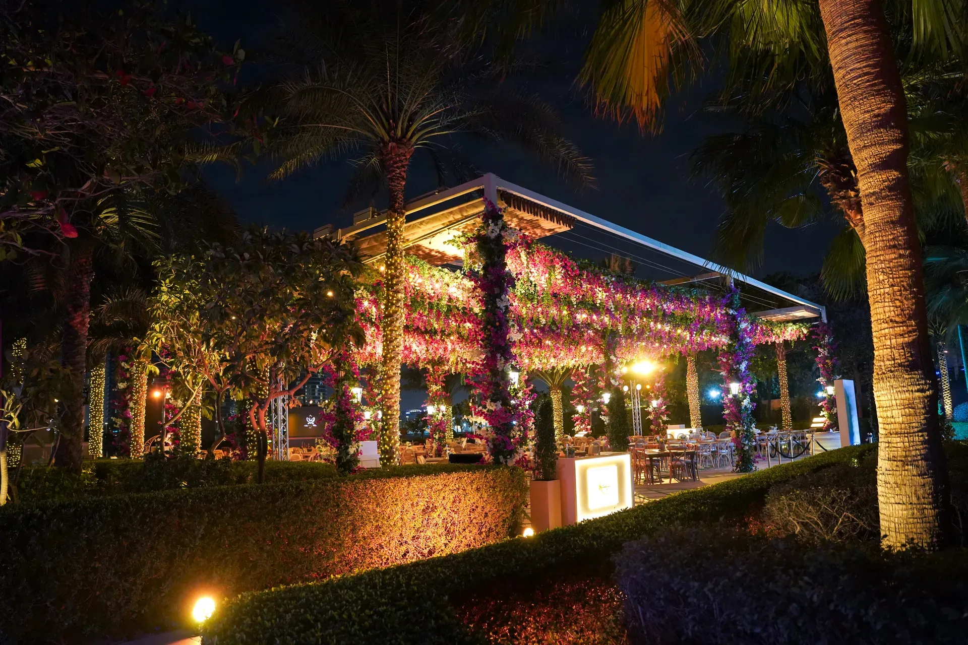 Garden pavilion with columns wrapped in pink blossom and lit at night