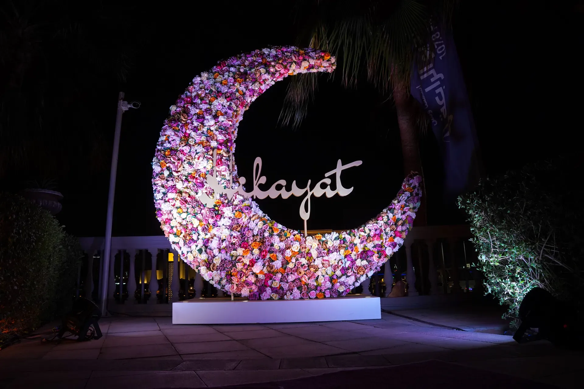 Large crescent moon sculpture covered in flowers and lit against a night garden