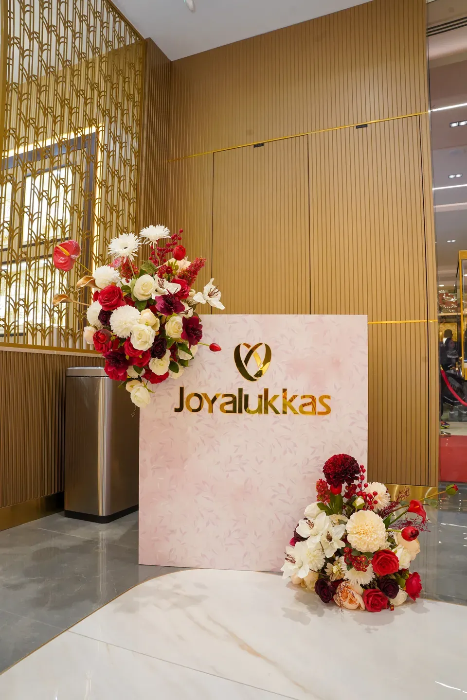Blush logo panel with red and white floral arrangements against a gold lattice wall