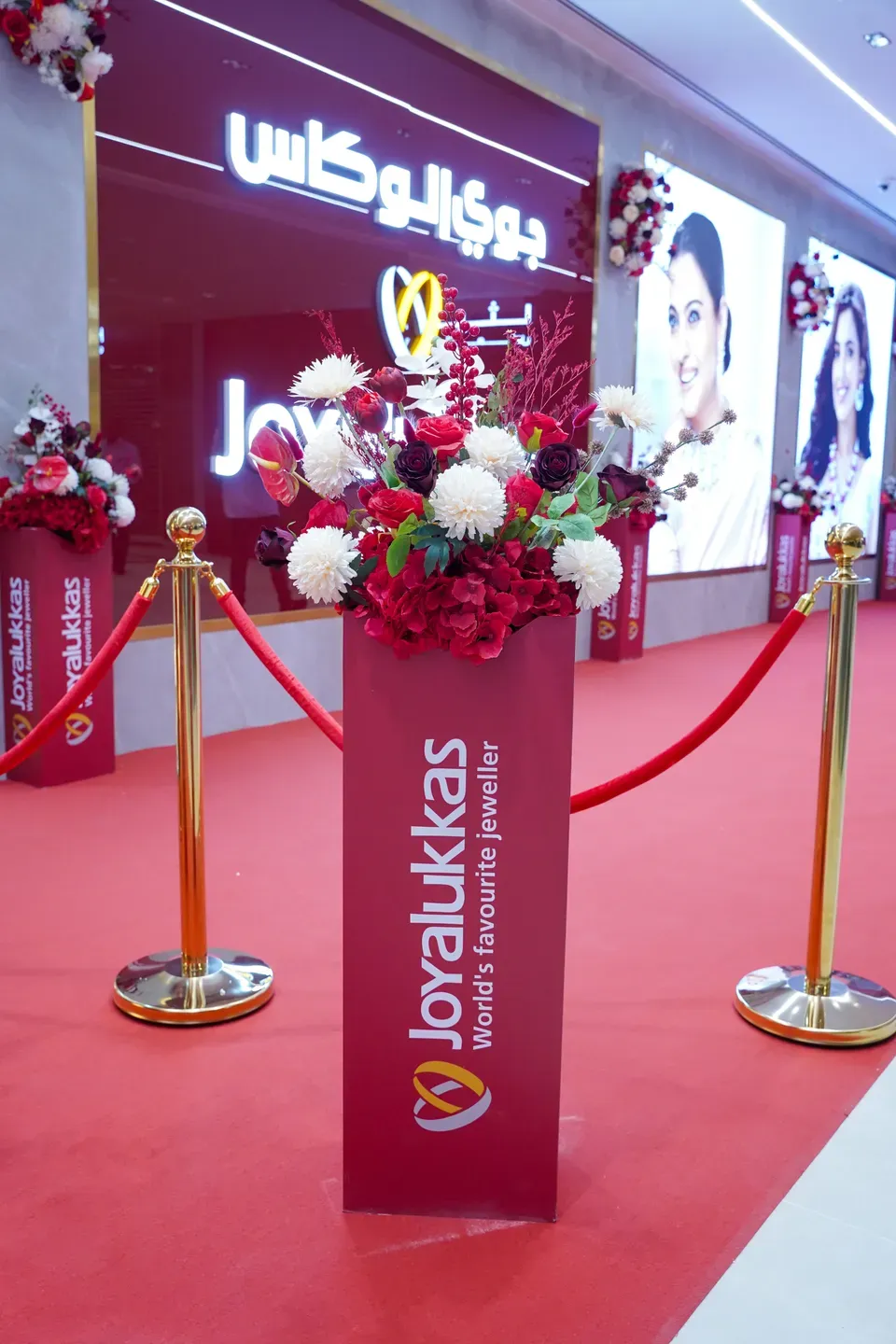 Branded plinth topped with red and white flowers between gold rope barriers on red carpet
