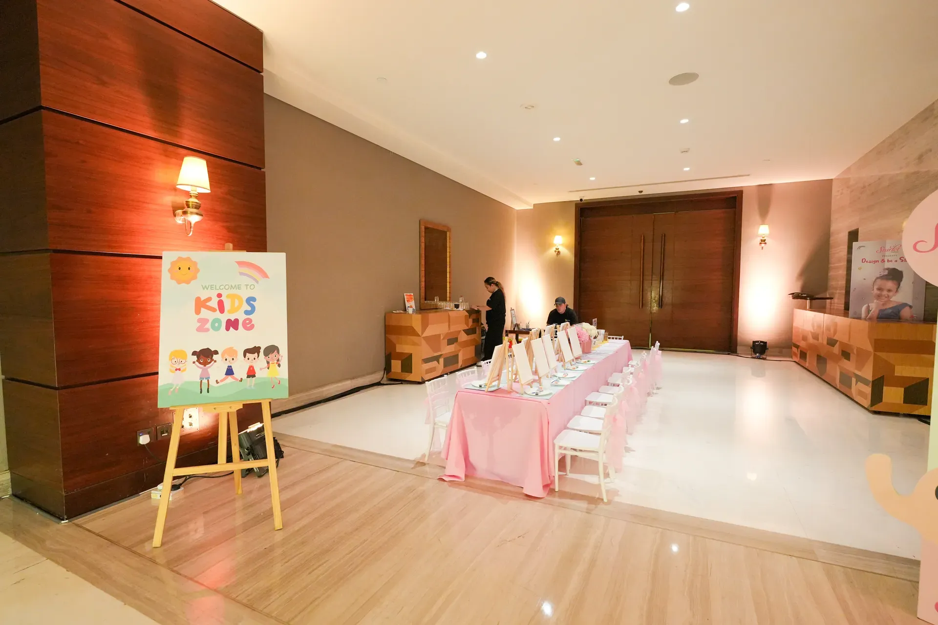 Pink children's table and chairs beside a Kids Zone easel sign in a hotel foyer