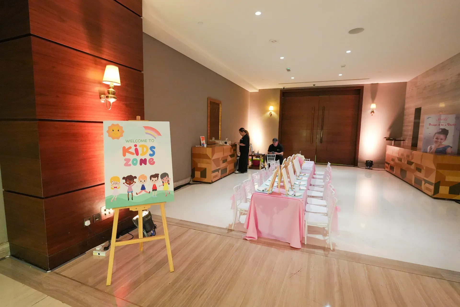 Pink kids table set with place settings beside a colourful easel sign
