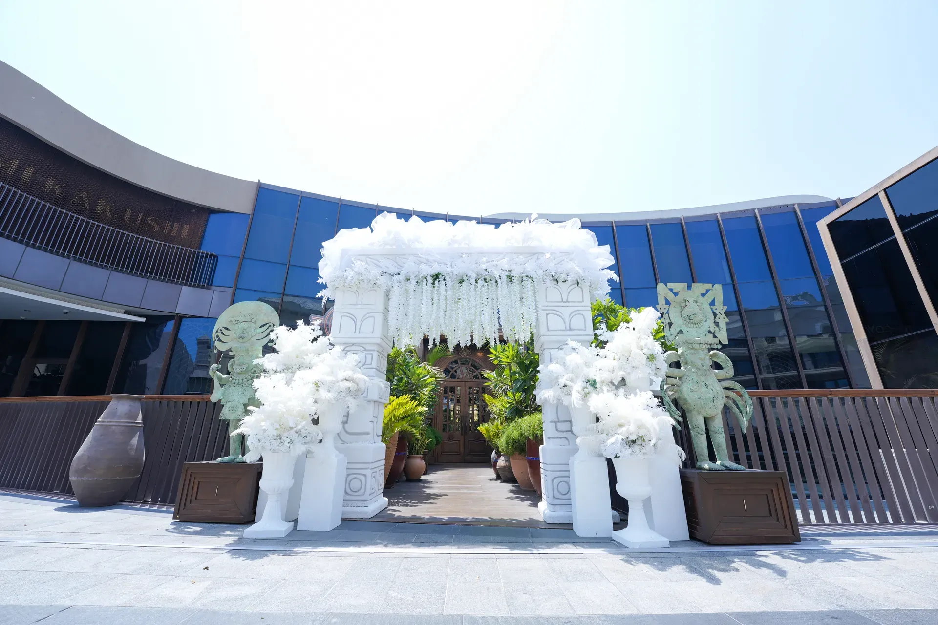 White floral entrance arch and guardian statues set up outside a glass-fronted venue