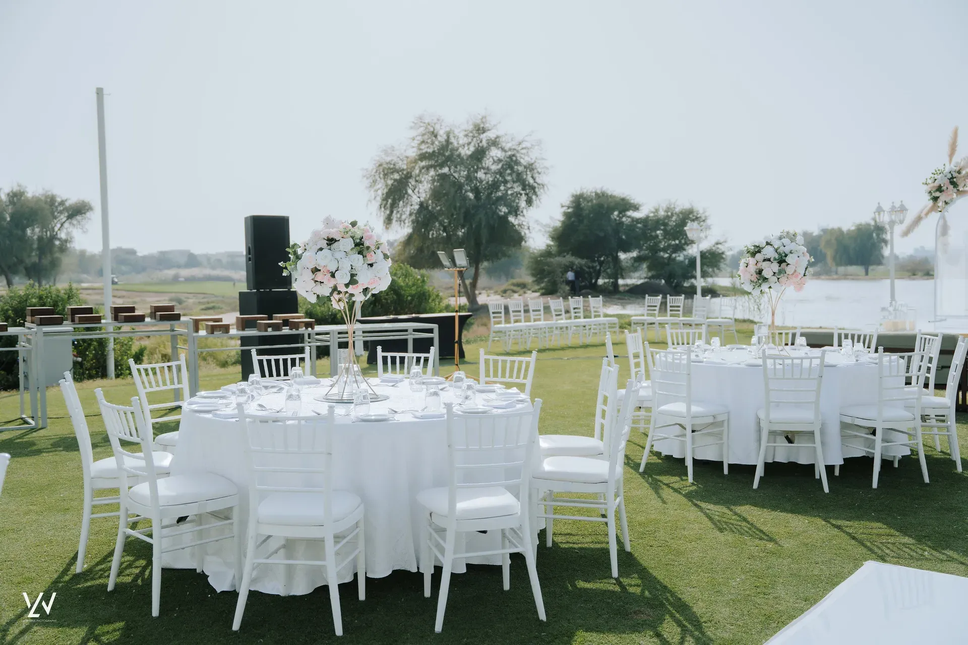 Round tables in white linen and chiavari chairs set on a lawn beside water