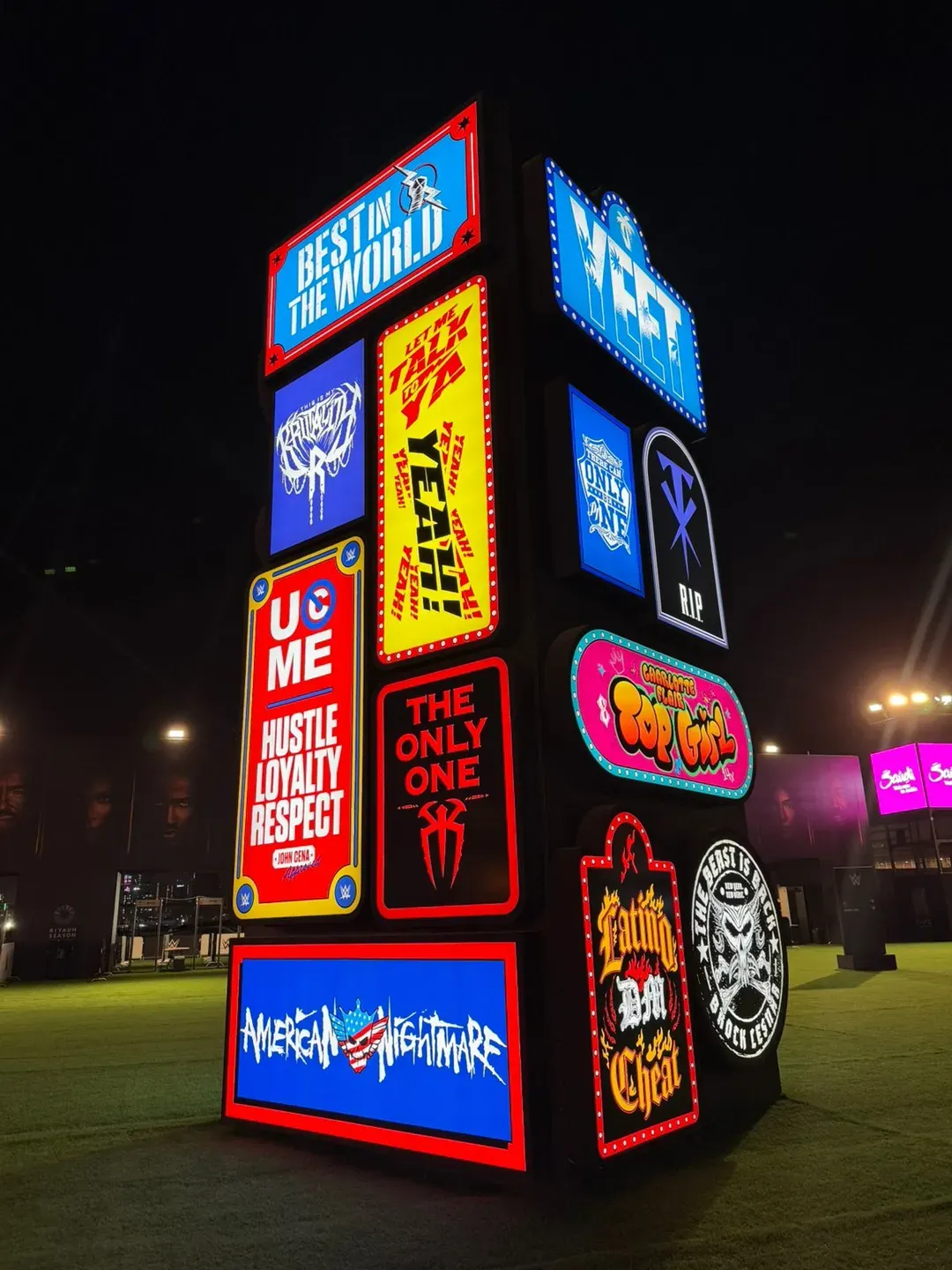Freestanding tower faced with illuminated slogan panels on a night lawn