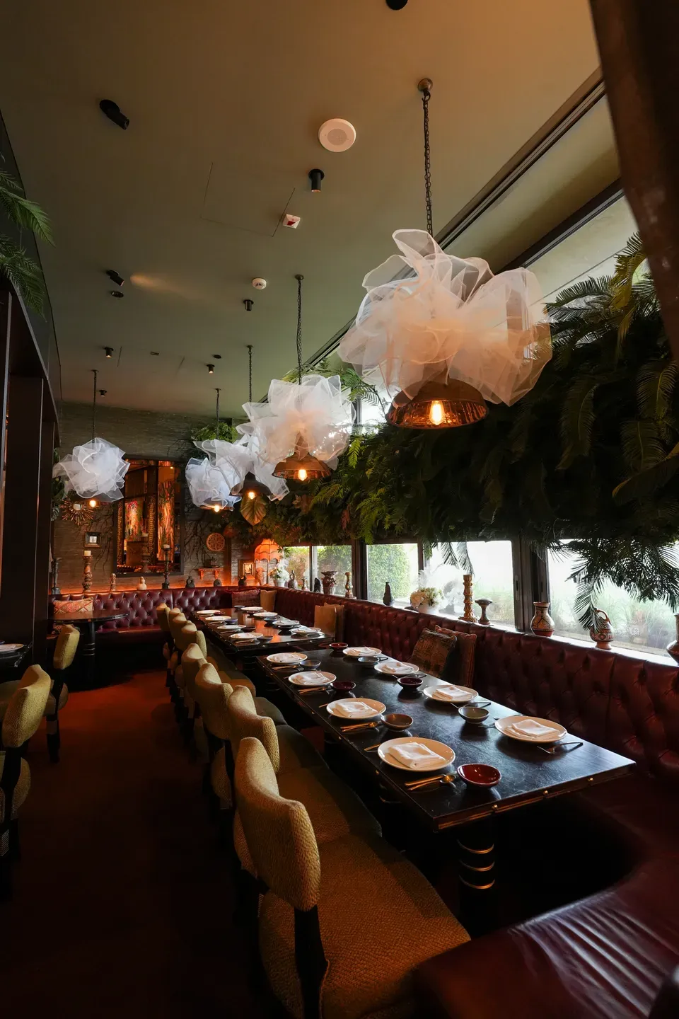 Long banquette table set for dinner beneath tulle puffs and hanging greenery