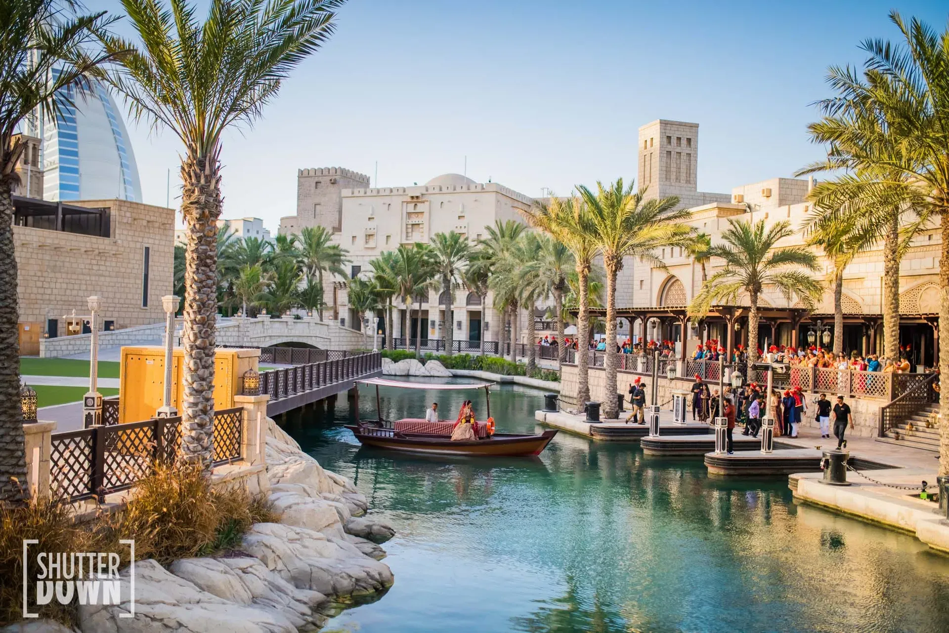 Wooden abra on a turquoise waterway between wind-tower buildings and palms