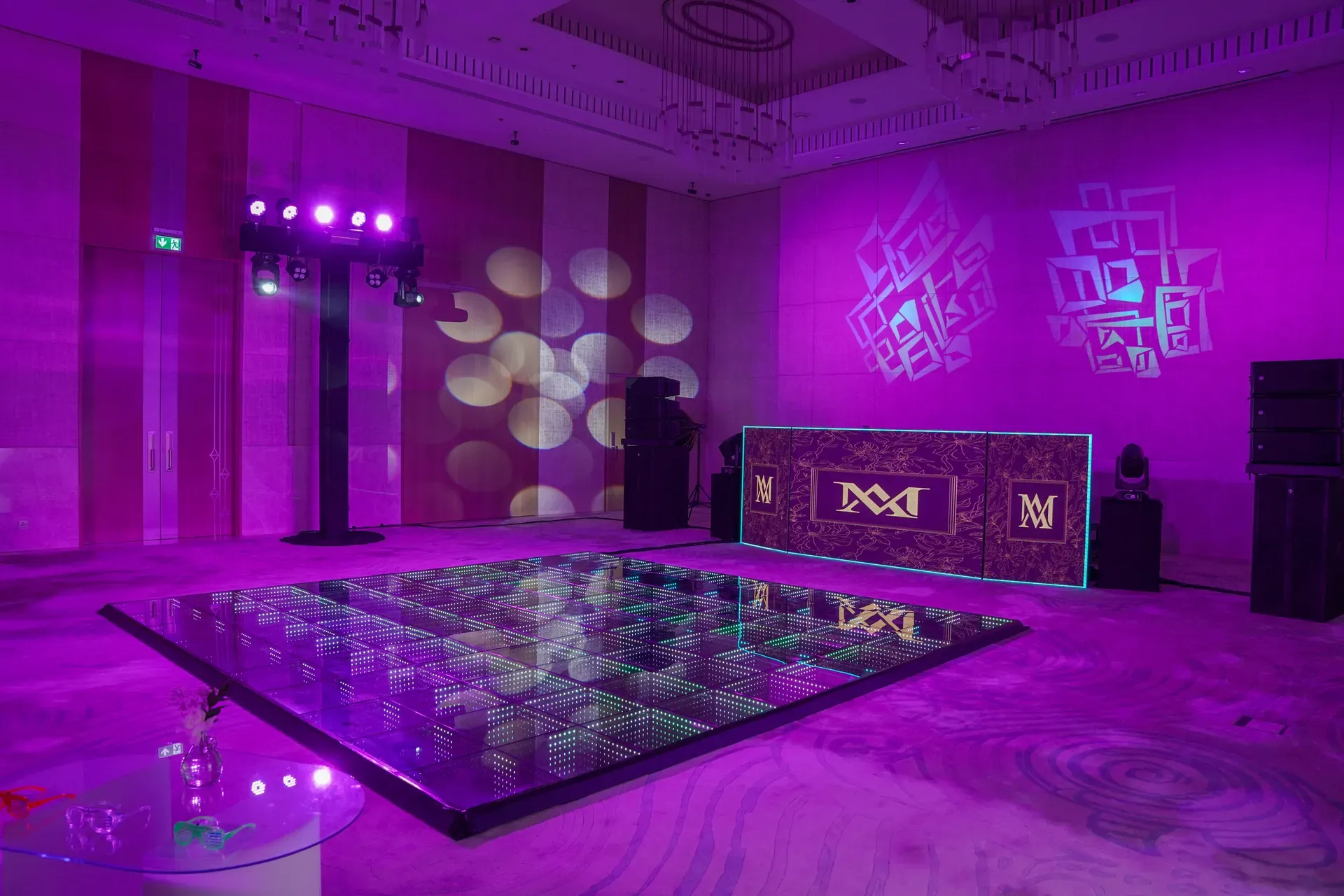 Mirrored dance floor in a ballroom washed magenta with a monogrammed bar and gobo pattern