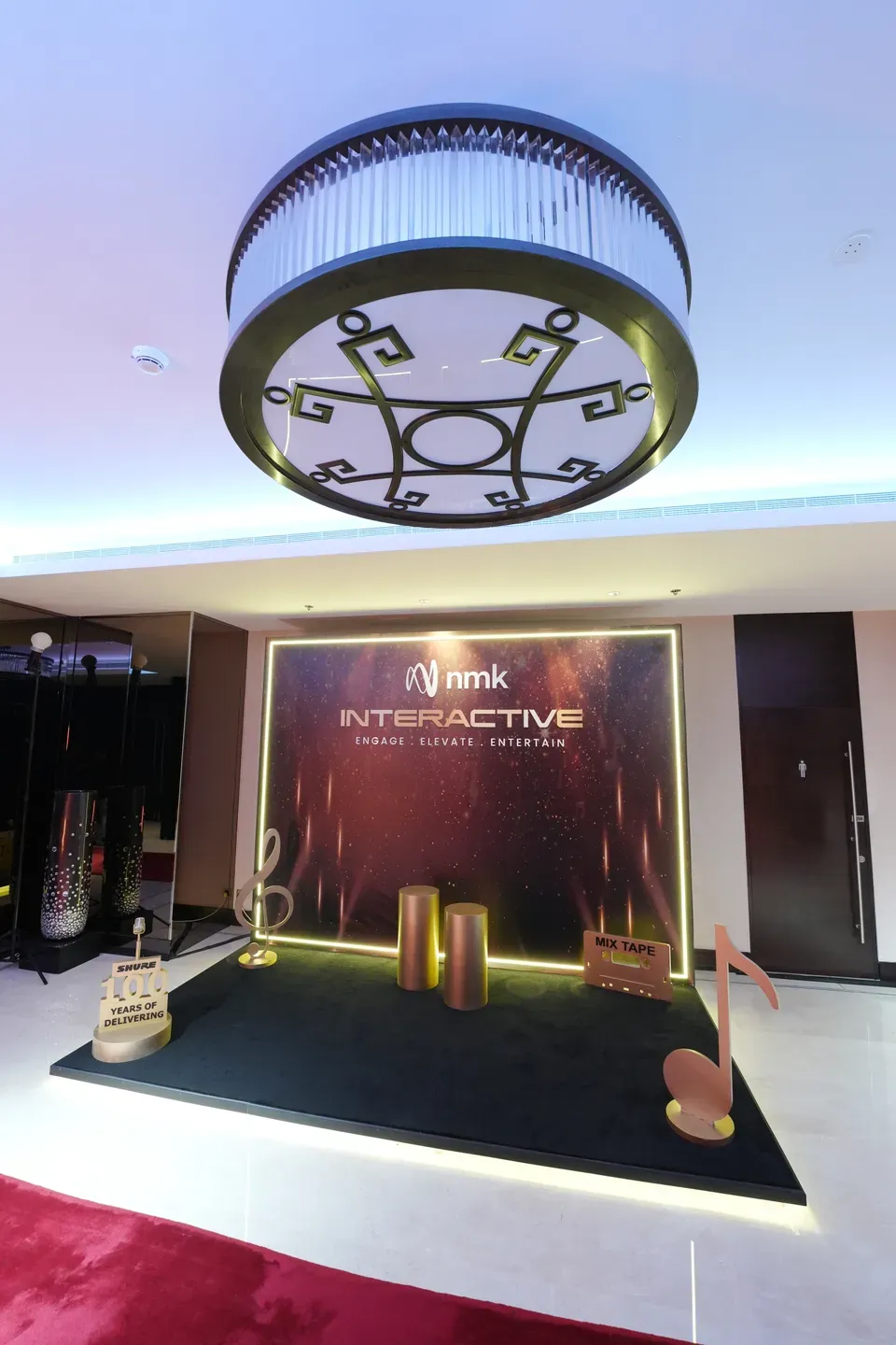 Dark branded backdrop and plinths under a circular truss ring in a hotel foyer