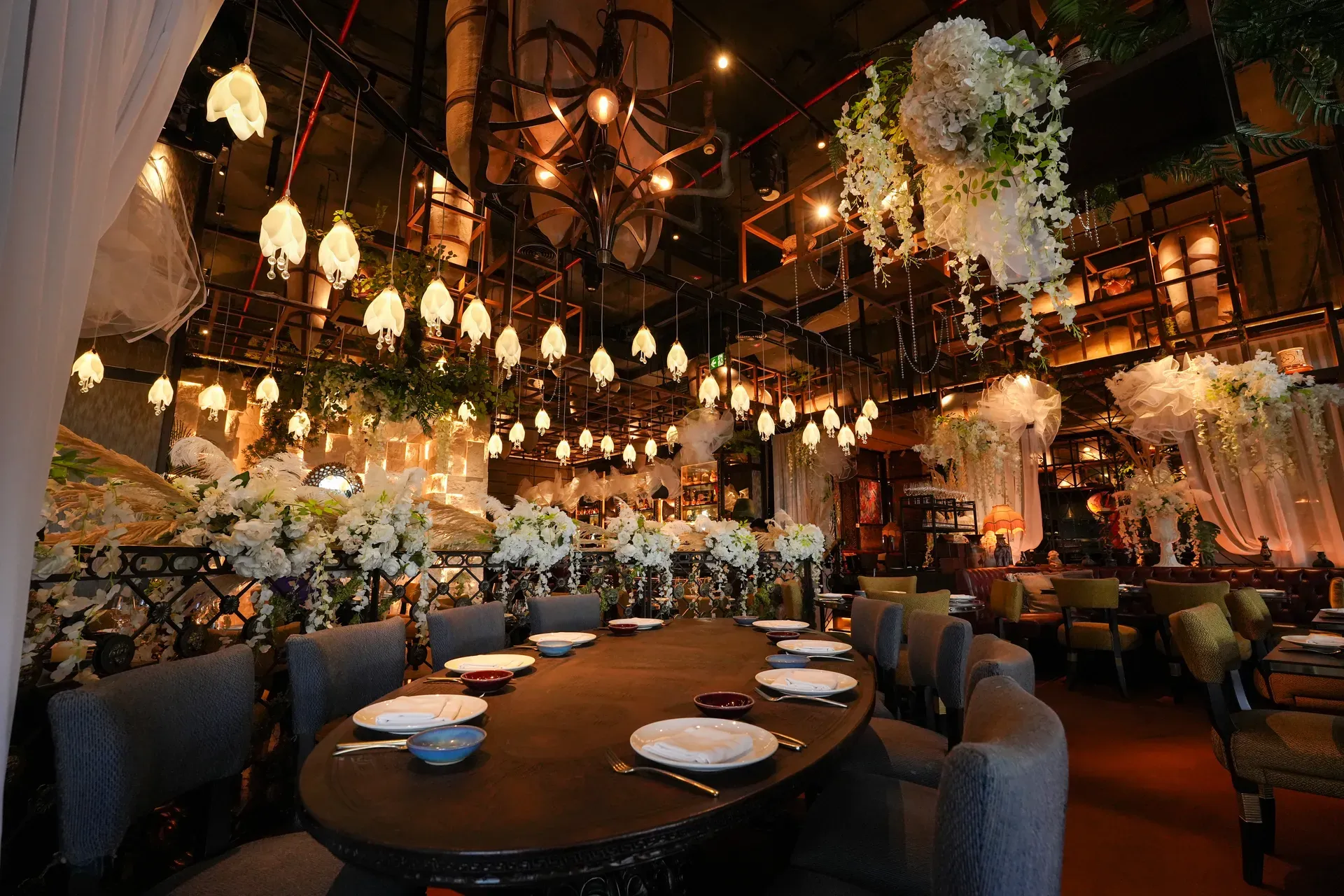 Round dining table below a cluster of glass pendants and cascading white florals