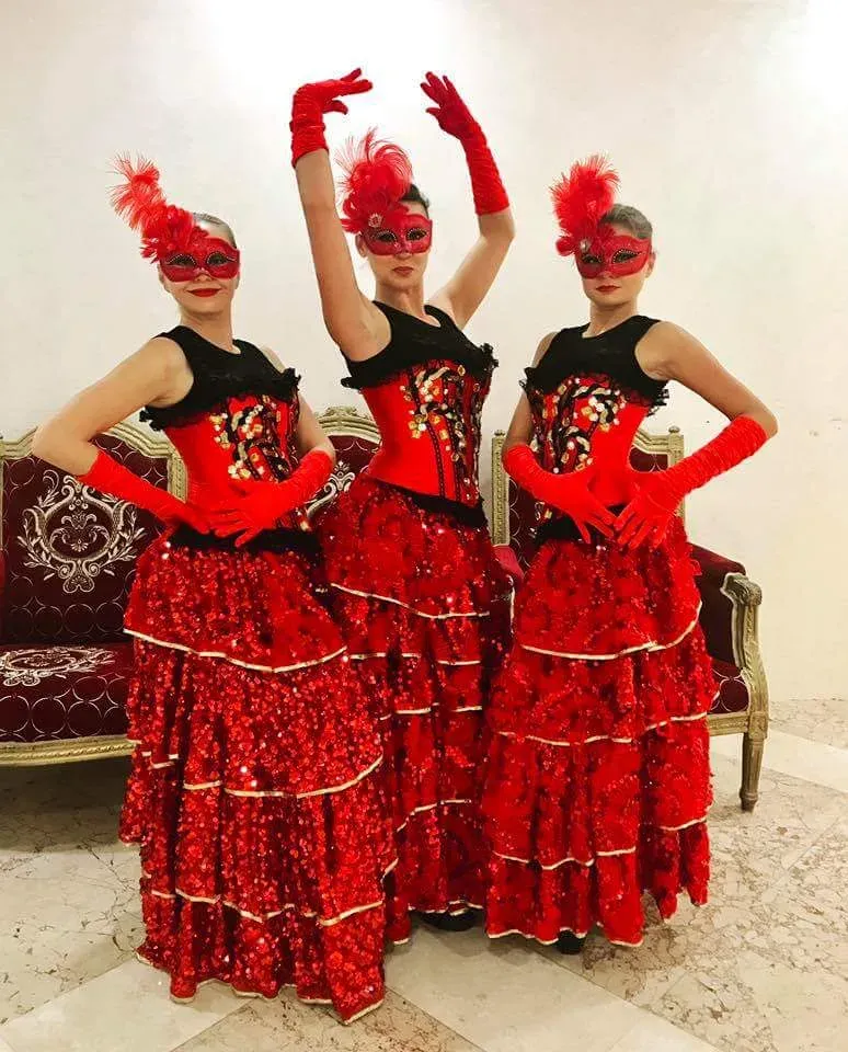 Three dancers in red ruffled gowns, gloves and feathered masks posed together
