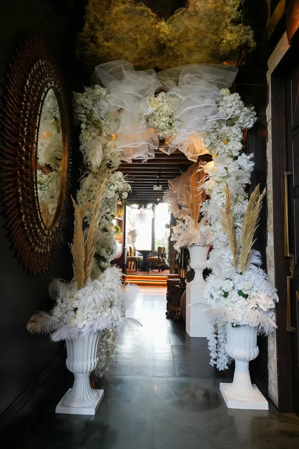 Two white urns of pampas and orchids framing a restaurant doorway hung with tulle