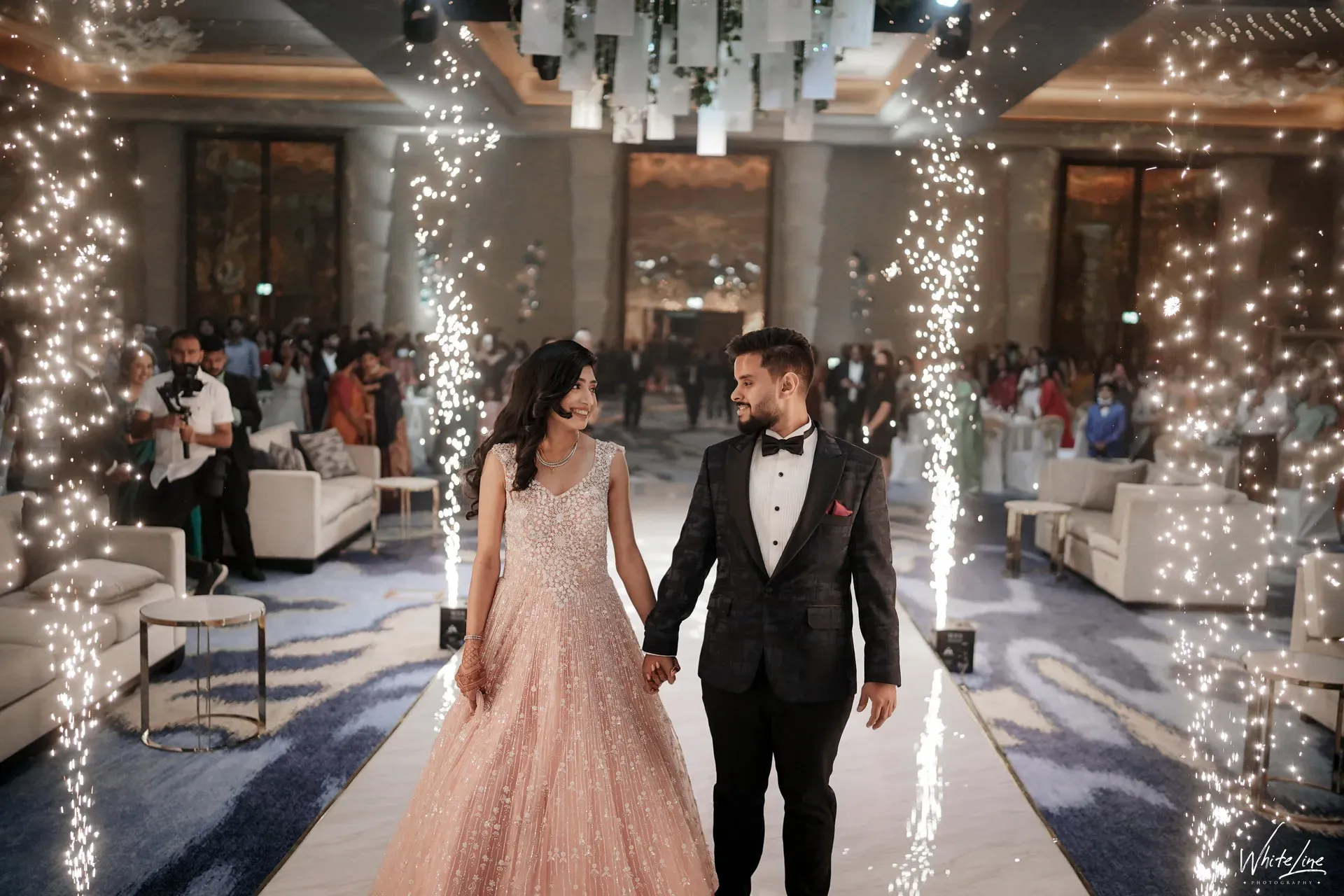 Couple walking hand in hand between two rows of cold-spark fountains into a hotel reception