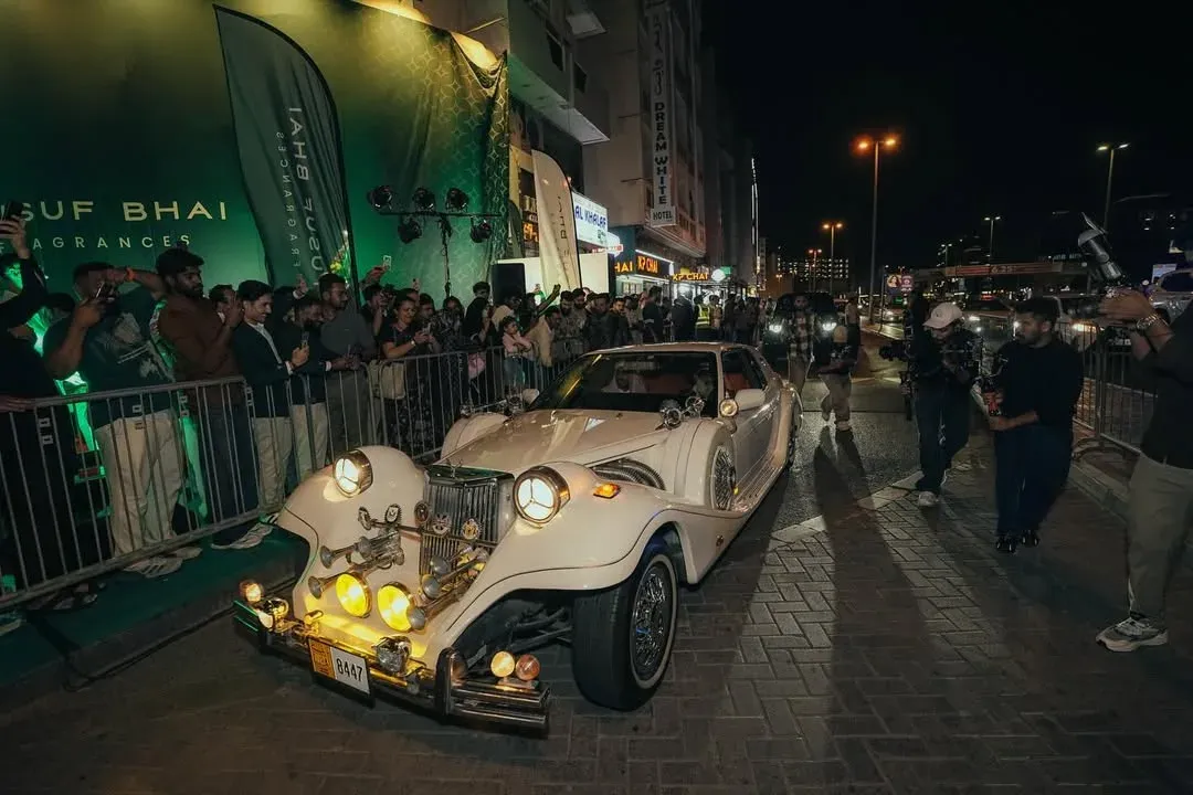 Vintage cream car parked before a crowd behind barriers at a night store opening