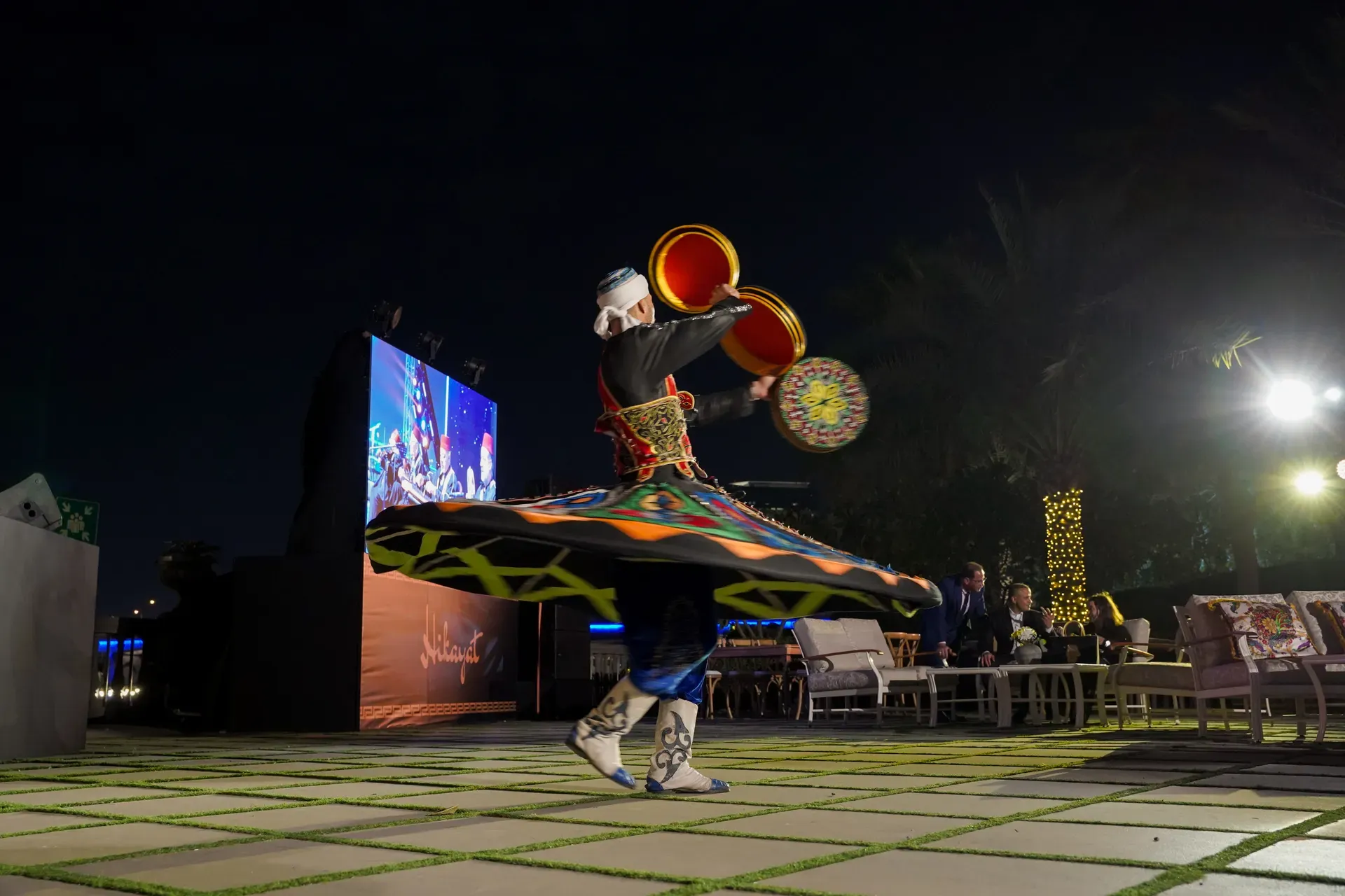 Tanoura dancer spinning with an illuminated patterned skirt raised on a terrace