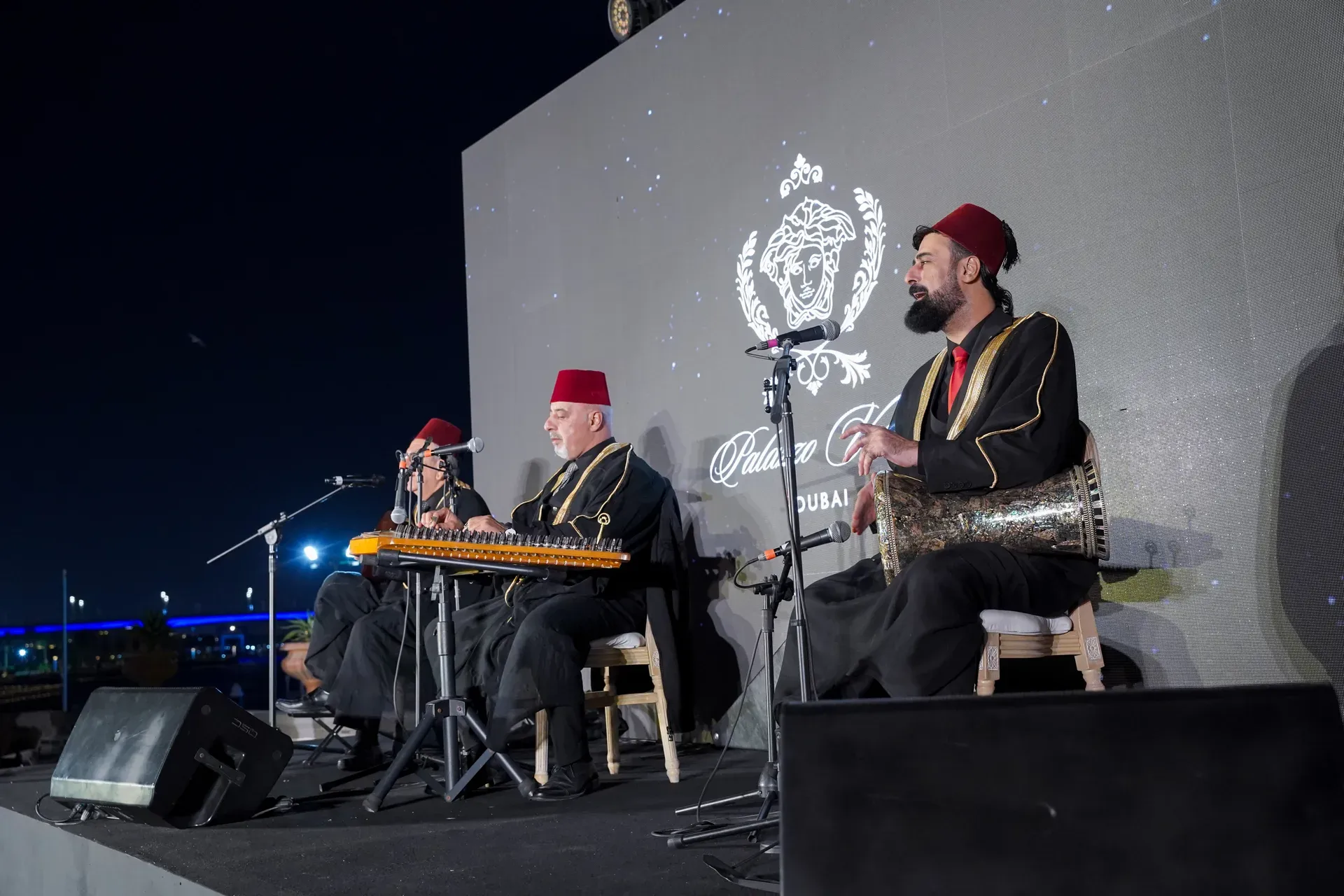 Three musicians in embroidered robes and red tarboosh hats playing qanun and drum