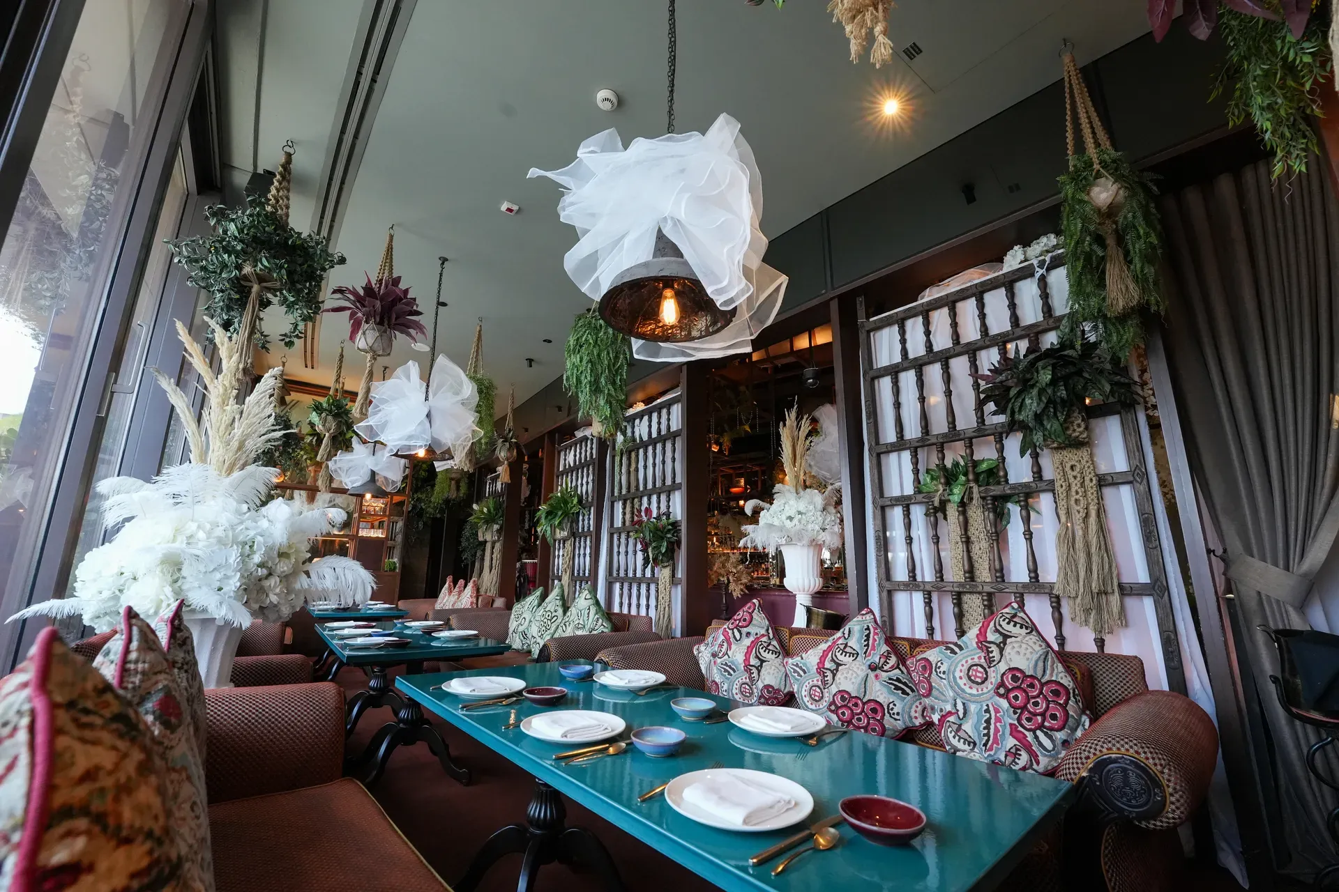 Teal banquet table set with patterned cushions beneath dried-grass and tulle installations