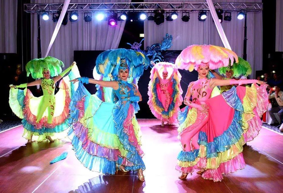 Group of dancers in bright ruffled costumes performing under coloured stage lights