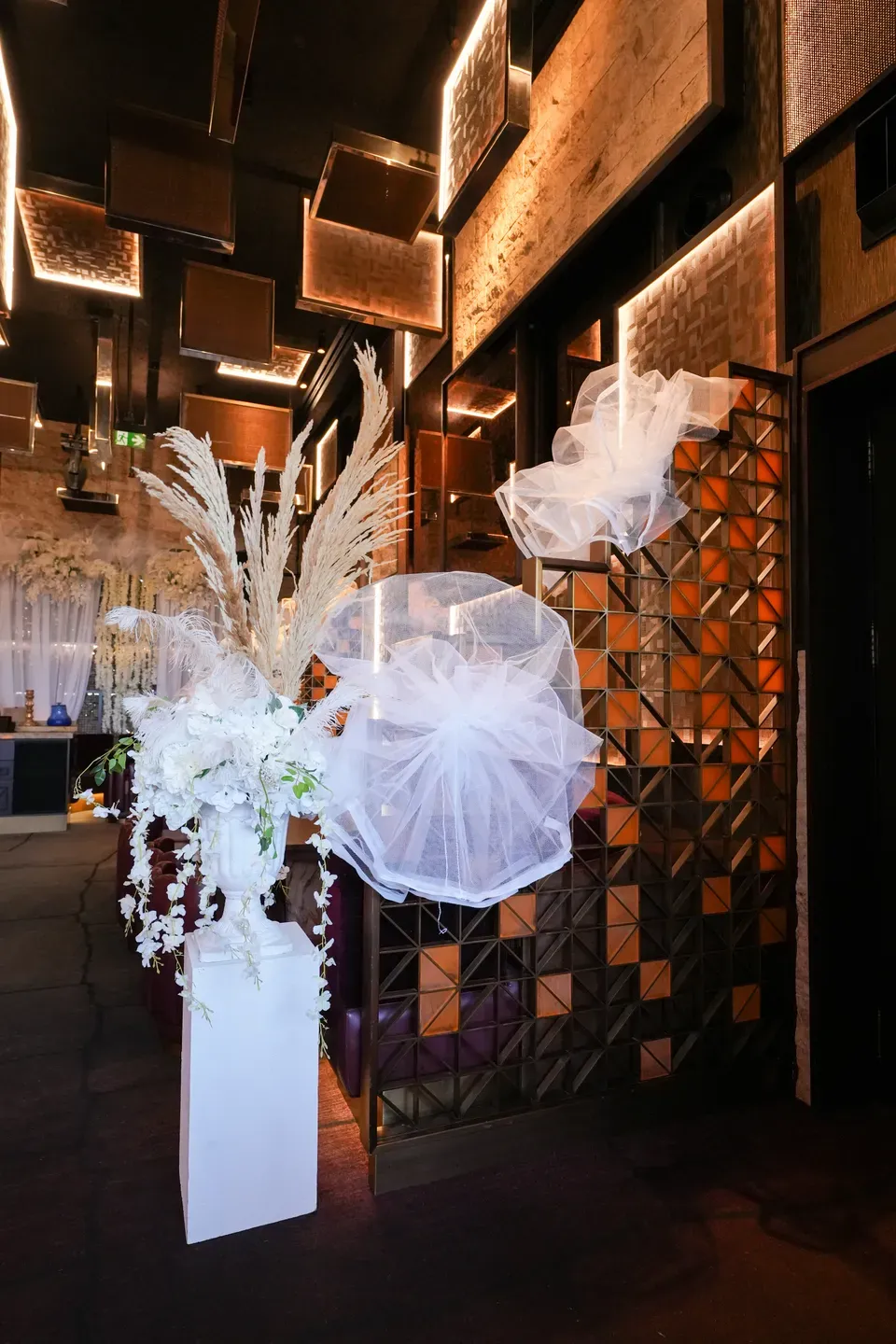 White plinth of pampas and orchids beside a tulle puff on a patterned tile wall
