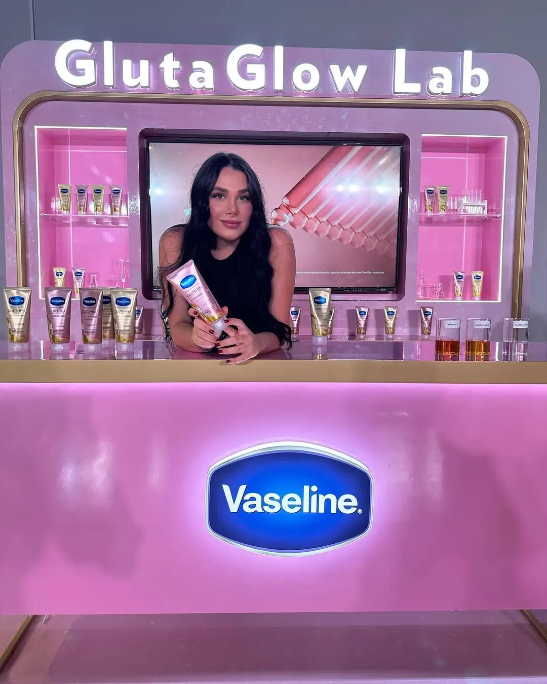 Branded pink counter with lit shelves of product and a screen behind