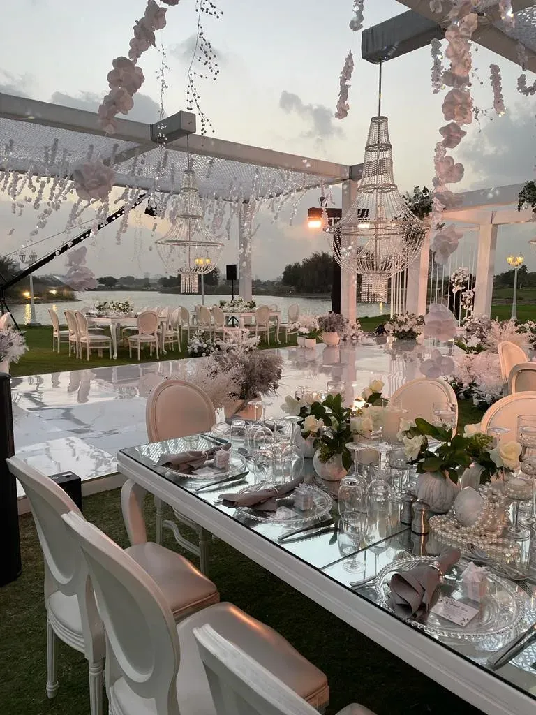 Mirror-topped banquet table under a pergola hung with blossom garlands and beaded chandeliers