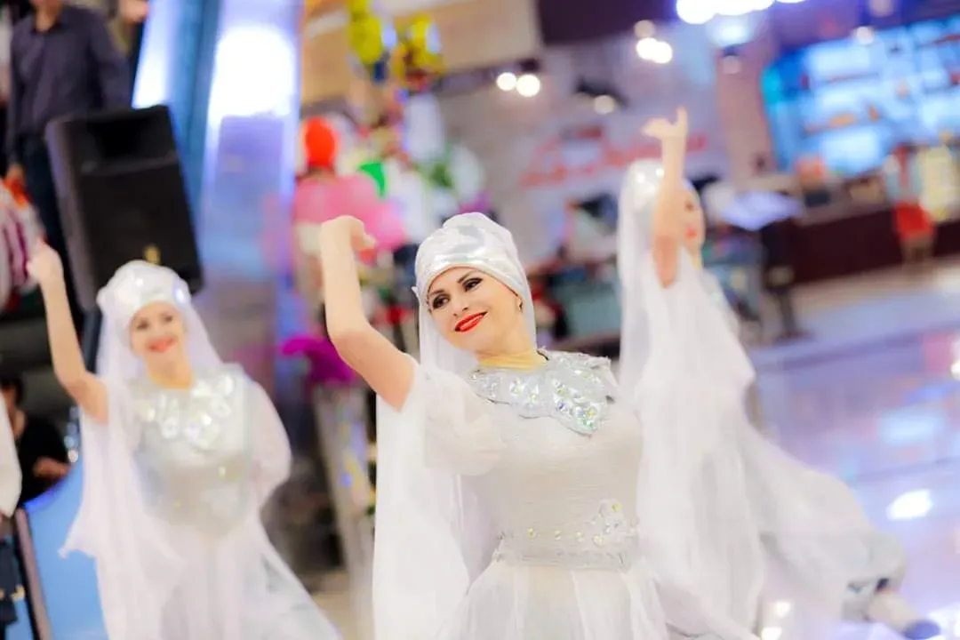 Dancers in white veiled costumes with arms raised performing indoors